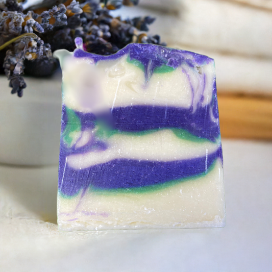 A bar of handmade lavender soap with swirls of purple, green, and white. The soap has a smooth texture and is displayed in front of a bundle of dried lavender flowers, suggesting a natural, calming scent.