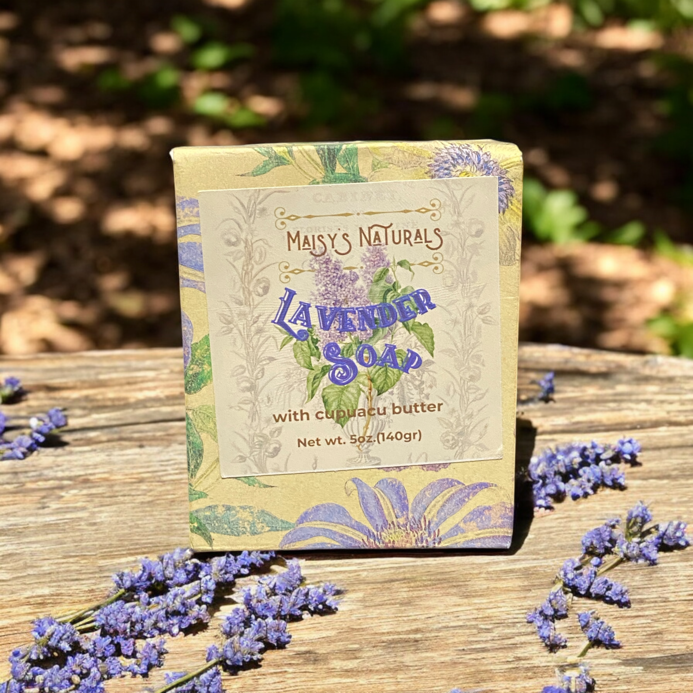 Maisy's Naturals Lavender Soap with cupuacu butter in a decorative floral box, resting on a rustic wooden surface surrounded by sprigs of fresh lavender. Captured outdoors in natural sunlight in Dallas, Arlington, Grand Prairie, Ft. Worth, Midlothian Tx.
